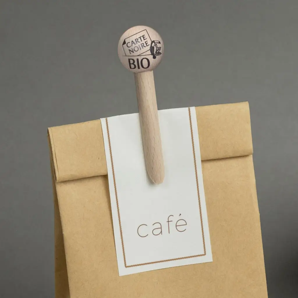 Pince à sachet en bois Pince-mi marquée au logo Carte Noire bio, fermant un sachet de café en papier kraft